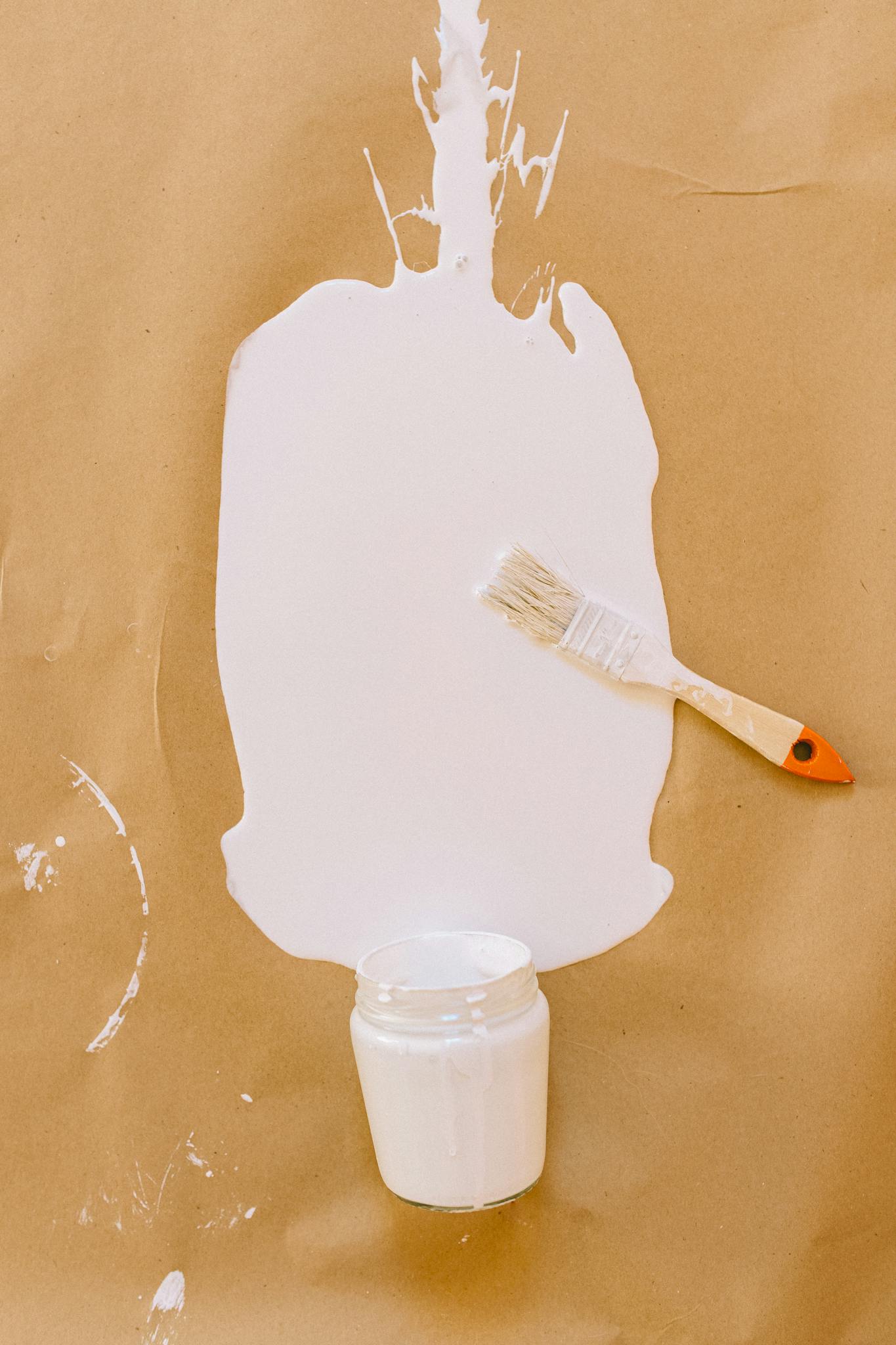 A brush beside a white paint spill on brown paper, showcasing a creative art setup.