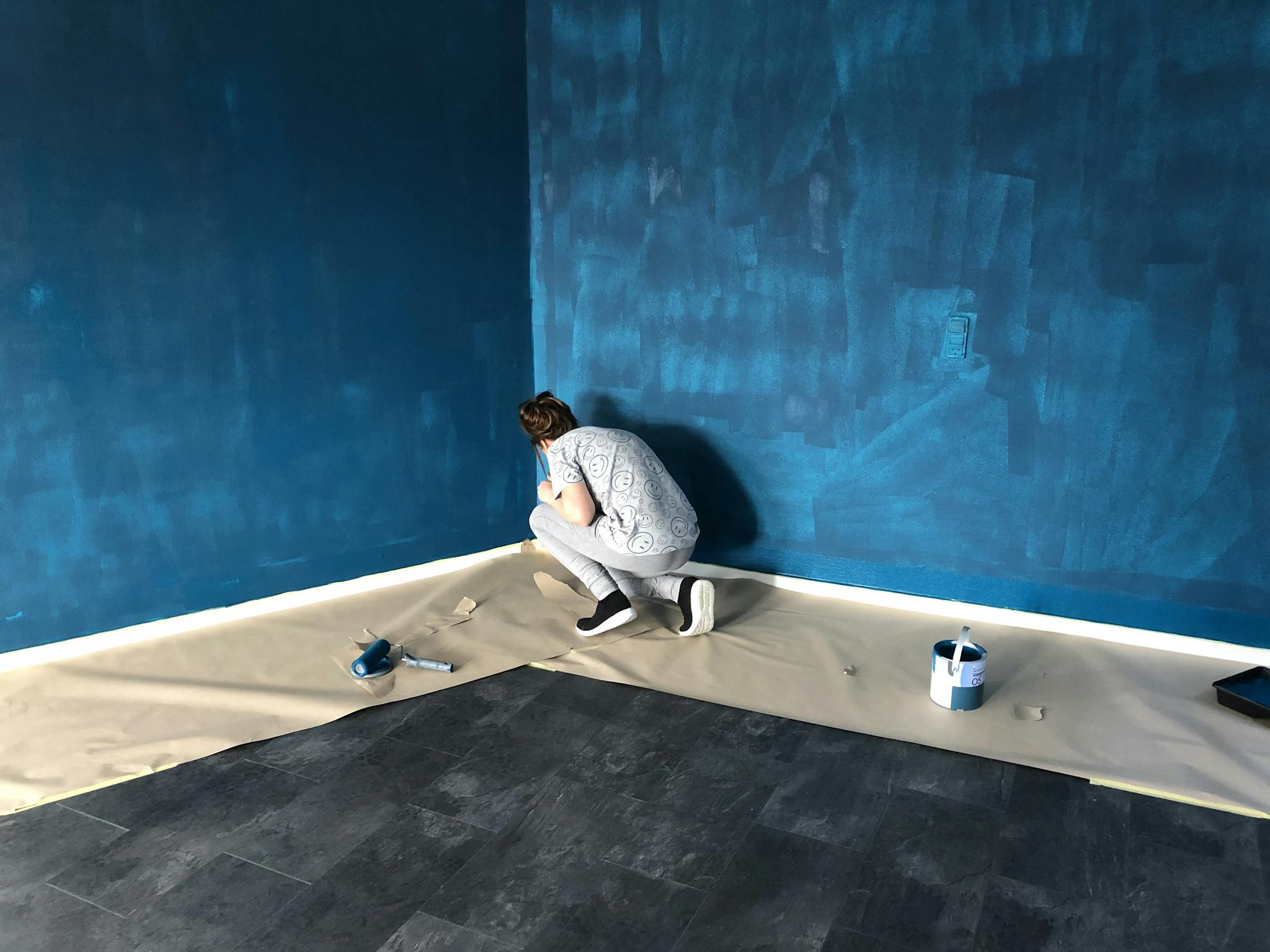 A woman painting a blue wall indoors for a home renovation project.